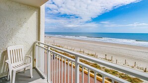 Ein Balkon mit Blick auf den Strand, ein weißer Stuhl und ein Geländer.