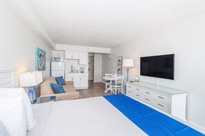 Ein Hotelzimmer mit Bett, Fernseher, Schreibtisch und einer Küchenzeile.