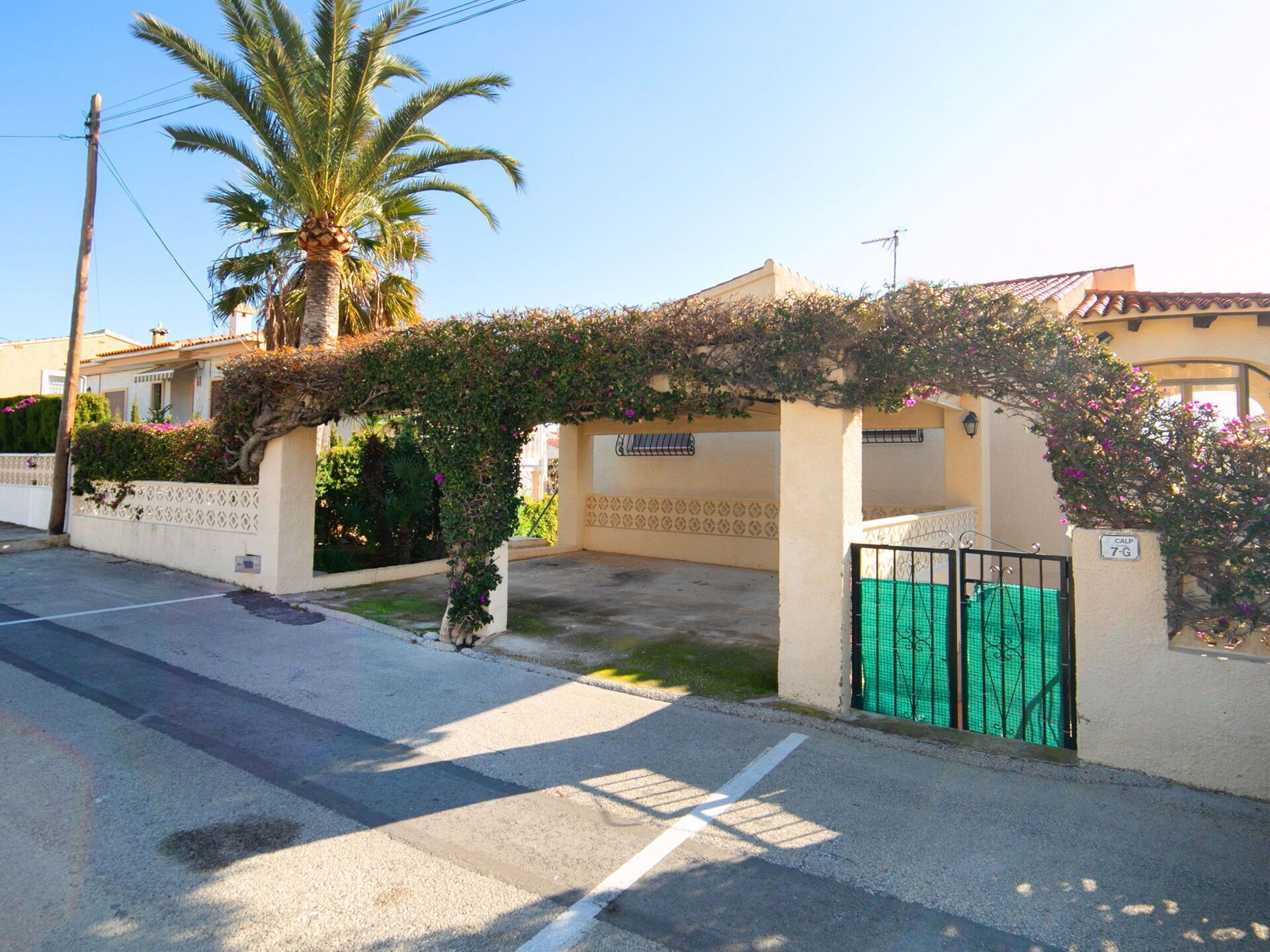 A residential area with a gated entrance, a palm tree, and a building with a tiled roof.