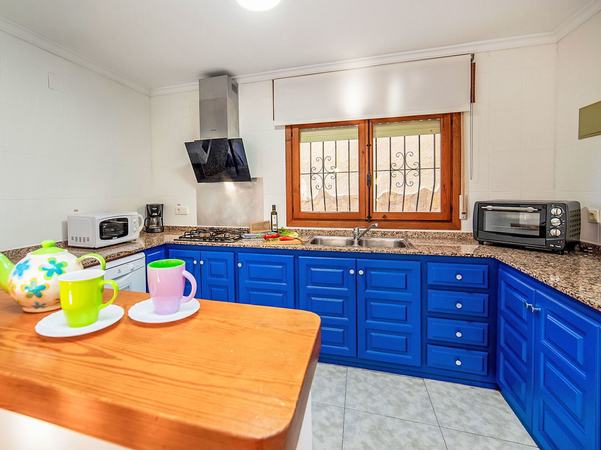 Een kleine keuken met blauwe kastjes, een gasfornuis, een magnetron en een broodrooster.