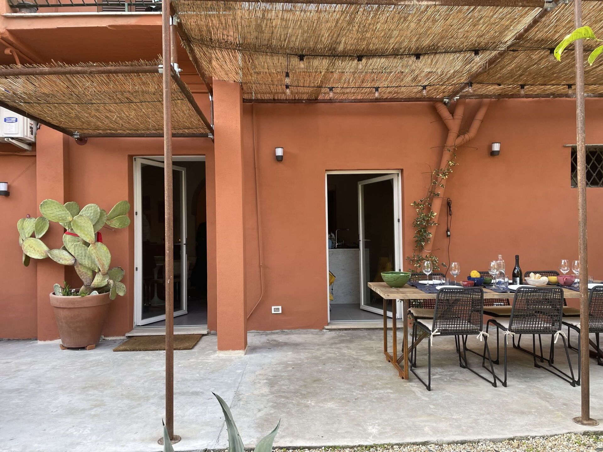 Un patio al aire libre con una mesa lista para comer, rodeado de sillas y una planta de cactus en maceta.