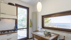 Een keuken met een gasfornuis, een eettafel met stoelen, een hanglamp en een raam met uitzicht op zee.