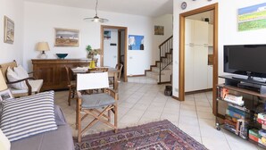 Een woonkamer met een bank, eettafel, stoelen, een televisie en een boekenkast.