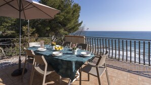Een tafel voor twee met uitzicht op zee, een terras met een balustrade en een boom op de achtergrond.