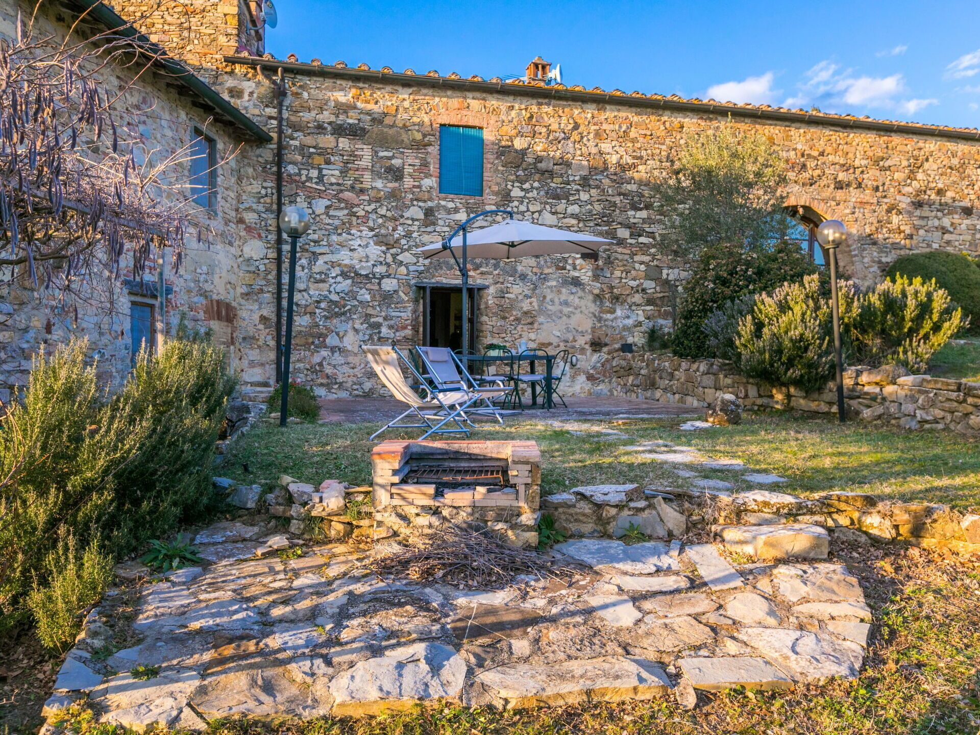Ein Steinhaus mit einer Terrasse, die einen Tisch und Stühle unter einer Markise bietet, umgeben von Steinmauern und Pflanzen.