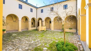 Un patio con suelo de adoquines, arcos y un árbol.