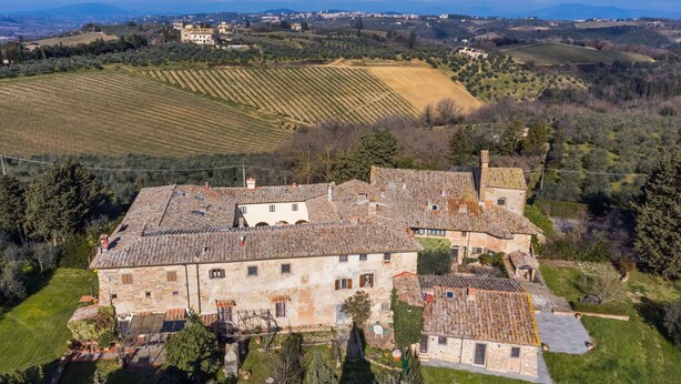 Vista aérea de un edificio histórico de piedra con varias construcciones, rodeado de viñedos en terrazas y colinas ondulantes.