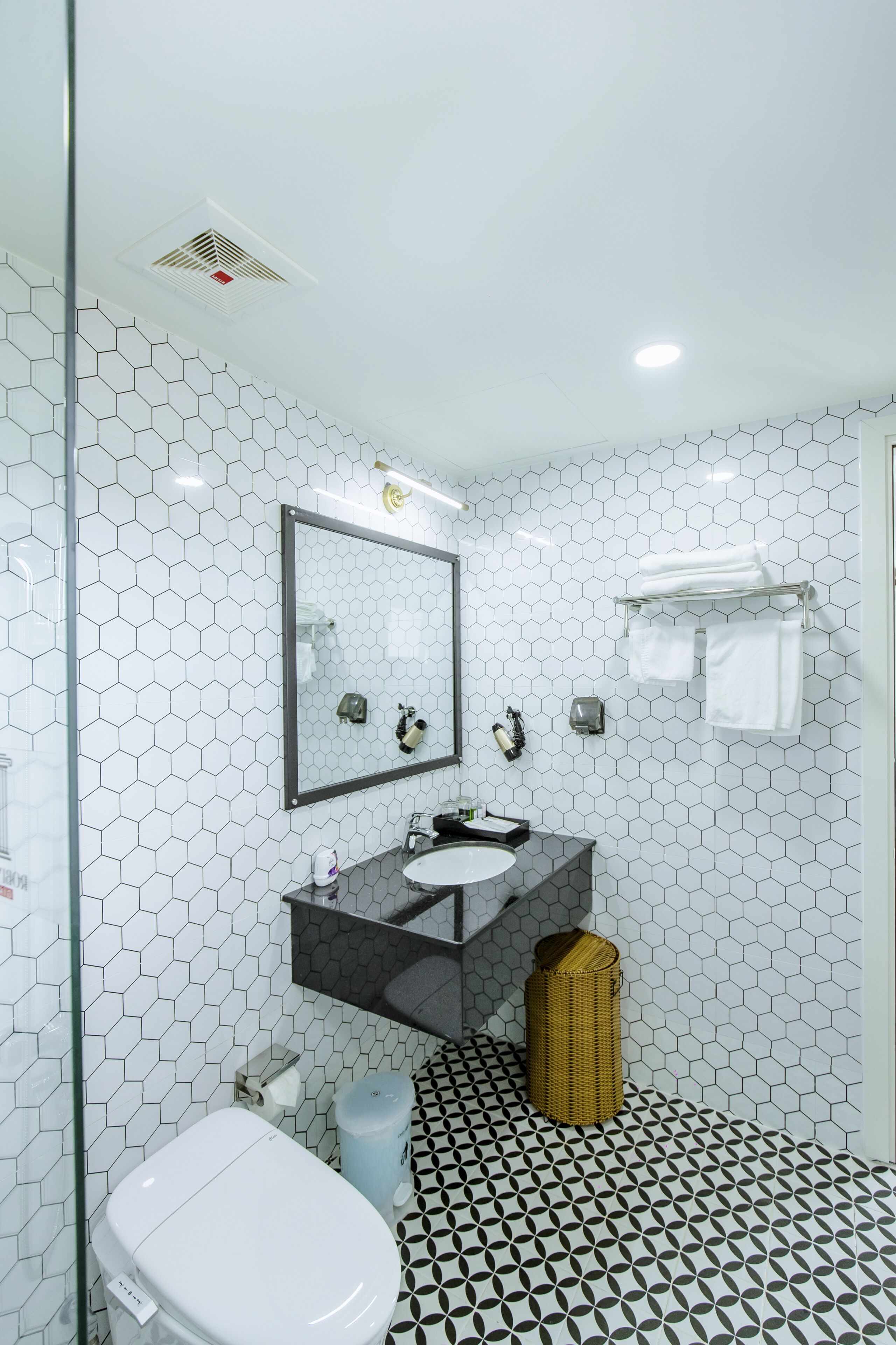 Une salle de bain avec un carrelage blanc à motifs hexagonaux, un grand miroir, un lavabo et des toilettes.
