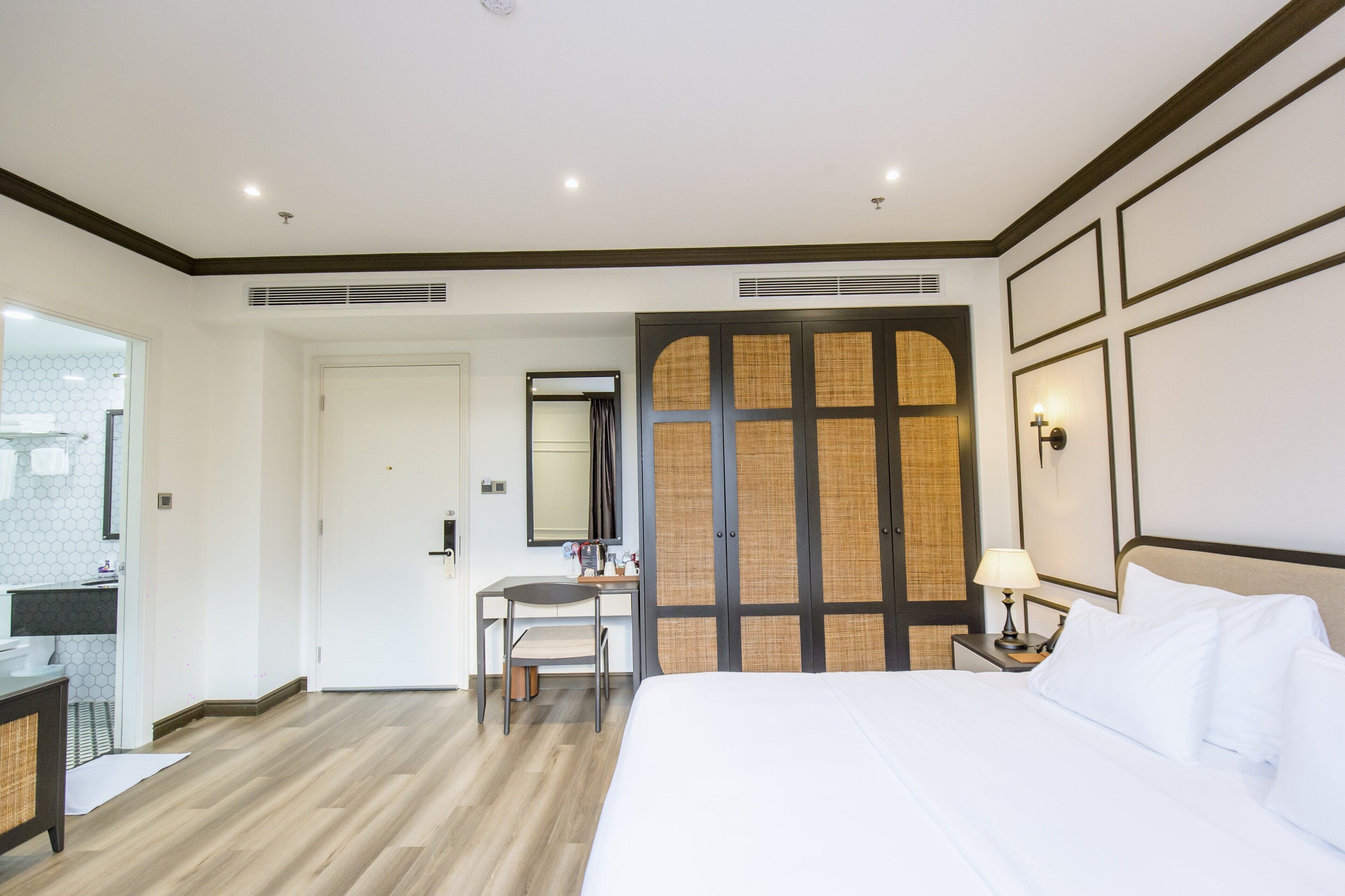 A hotel room with a bed, a desk, a chair, a mirror, and a wardrobe.