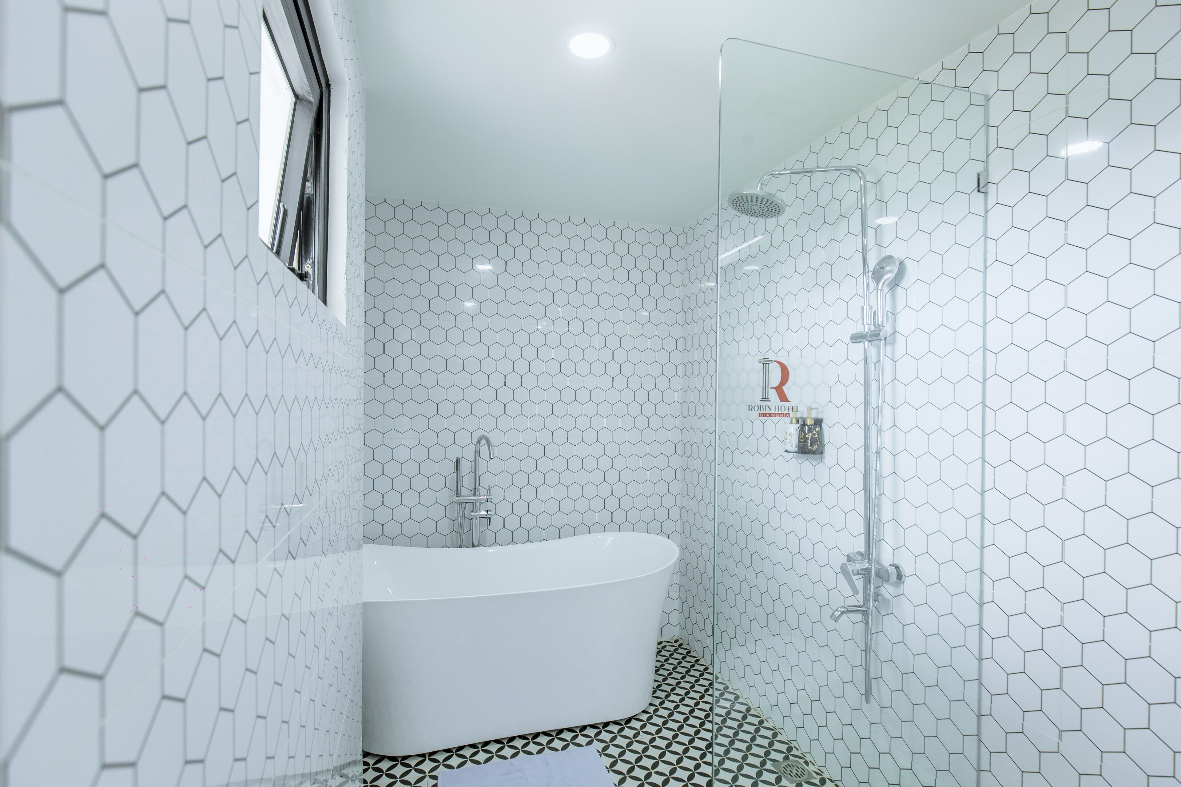 A modern bathroom with a hexagonal tile pattern, a freestanding bathtub, and a glass-enclosed shower area.