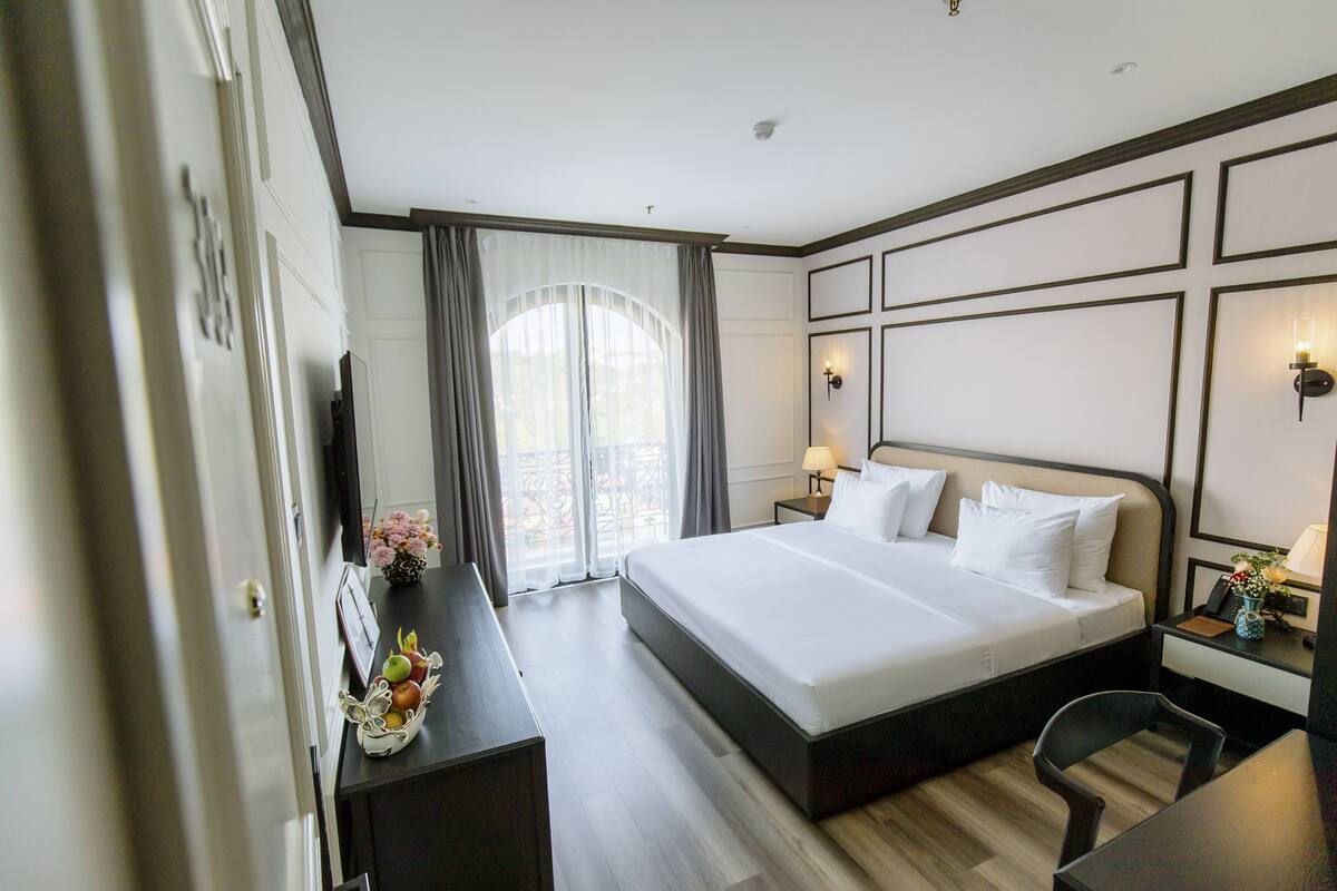 A hotel room with a large bed, a desk with a chair, a TV, and a window with curtains.