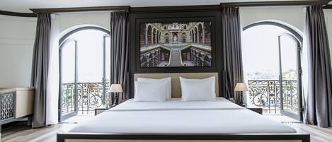 Una cama grande con cabecera, dos mesitas de noche con lámparas y un cuadro grande enmarcados sobre la cama.