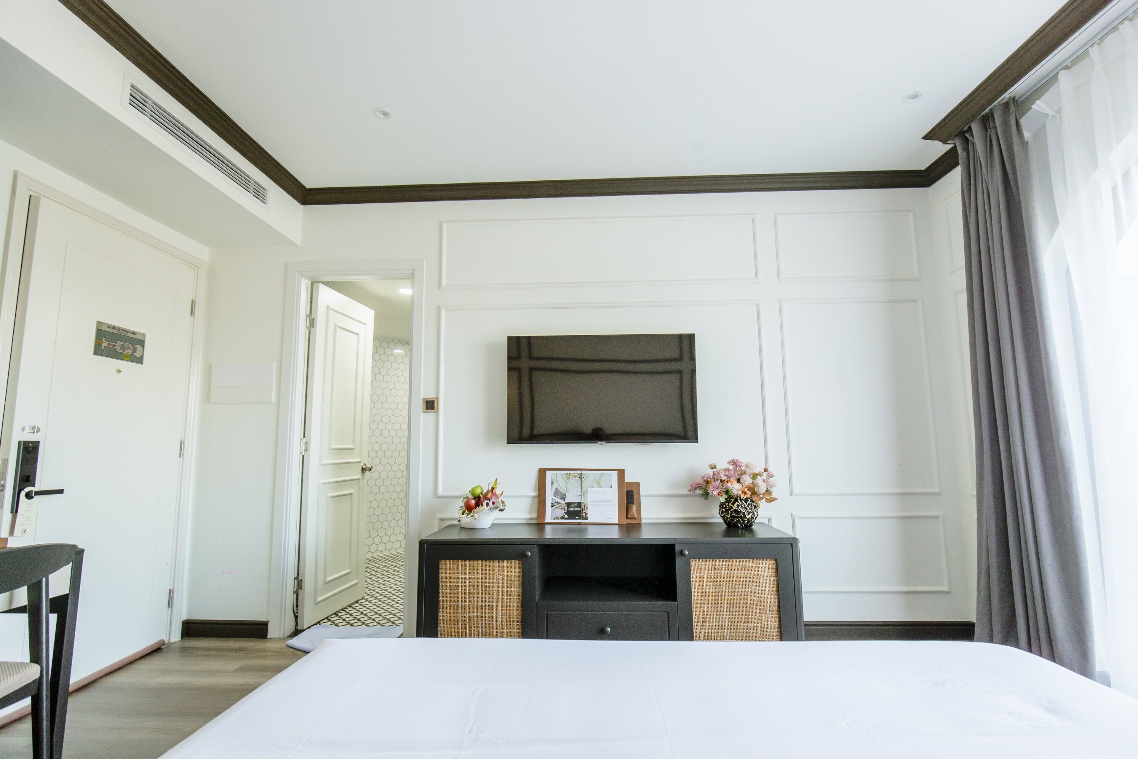 Une chambre d’hôtel avec un lit, un téléviseur fixé au mur, une commode et une porte donnant sur une autre pièce.