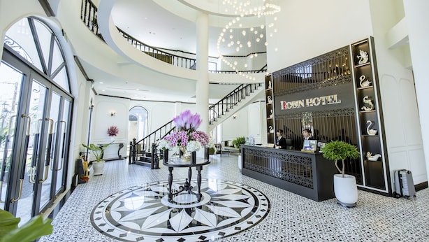 A hotel lobby with a central staircase, a reception desk, and a decorative floor pattern.