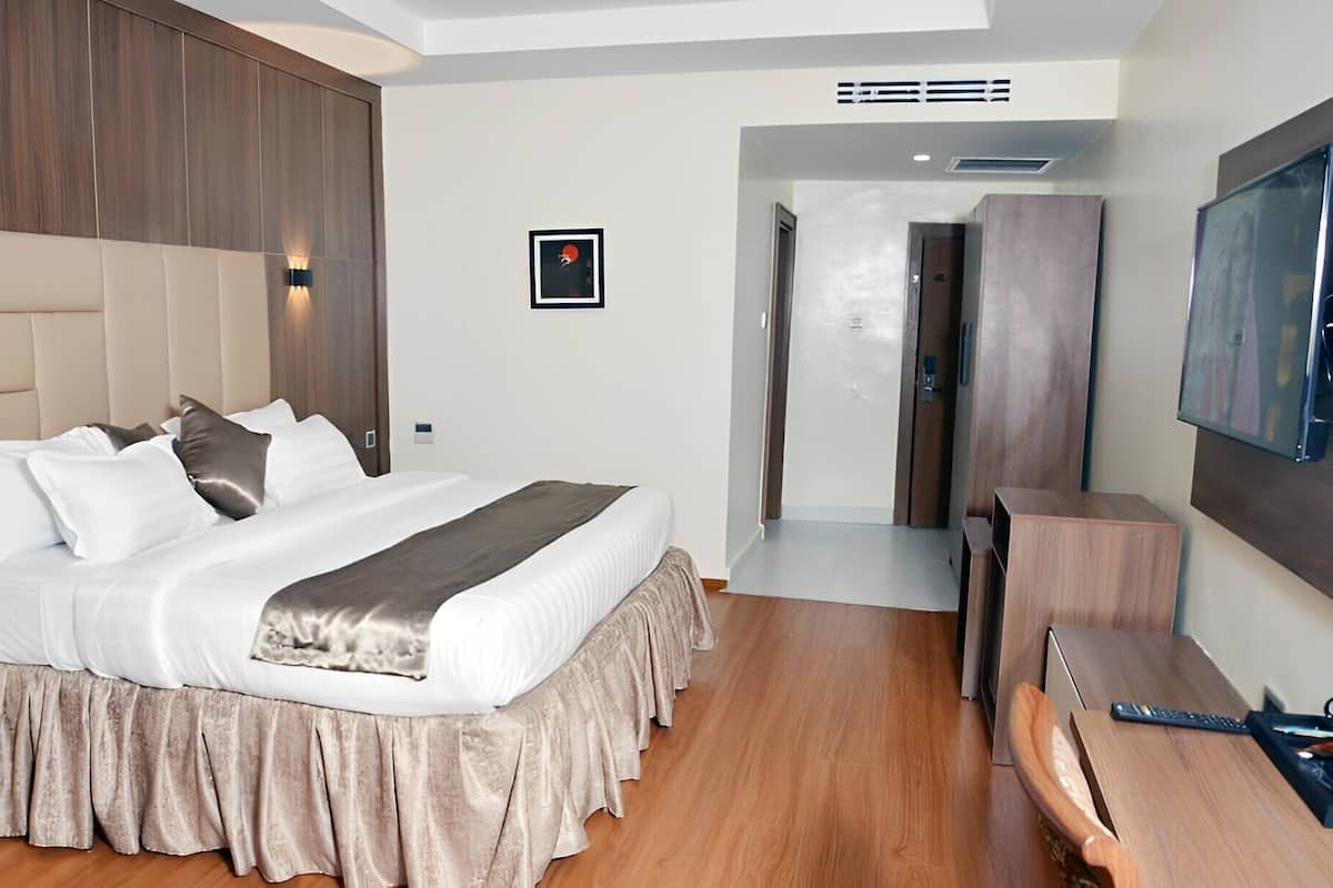 Een moderne hotelkamer met een groot bed, een bureau, een televisie en een deur naar een gang.