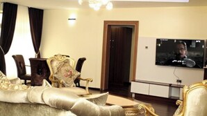 Un salon luxueux avec un canapé moelleux, des fauteuils élégants, un lustre et un téléviseur à écran plat fixé au mur.