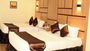 Une chambre d’hôtel avec deux lits, chacun doté d’une tête de lit marron, de draps blancs et d’un plaid marron. Des lampes murales et un tableau encadré ornent le mur.