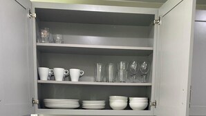Une cuisine équipée d’un évier à deux bacs, d’une machine à café et d’un placard contenant de la verrerie et de la vaisselle.