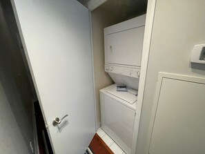 A compact laundry room with a white washing machine and dryer, a small shelf, and a door with a silver handle.