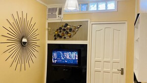 Ein Wohnzimmer mit Fernseher, Wanddeko, einer Deckenleuchte und einer Tür.