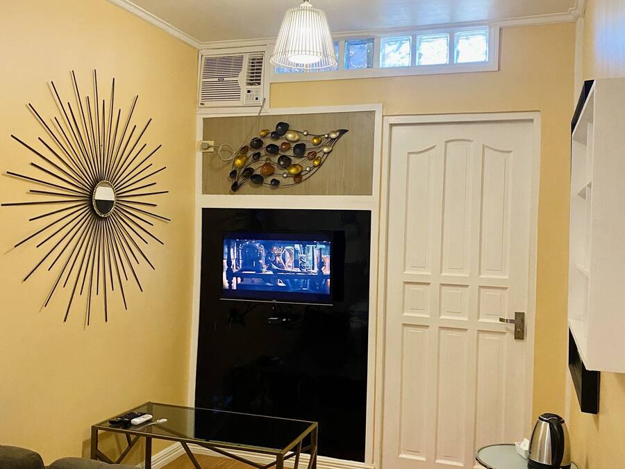 A living room with a television, a decorative wall piece, a chandelier, and a door.