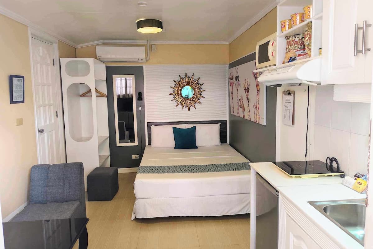 Une chambre d’hôtel de taille réduite, comprenant un lit, un bureau, une chaise, un miroir et un climatiseur fixé au mur.