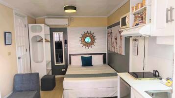 Une chambre d’hôtel de taille réduite, comprenant un lit, un bureau, une chaise, un miroir et un climatiseur fixé au mur.