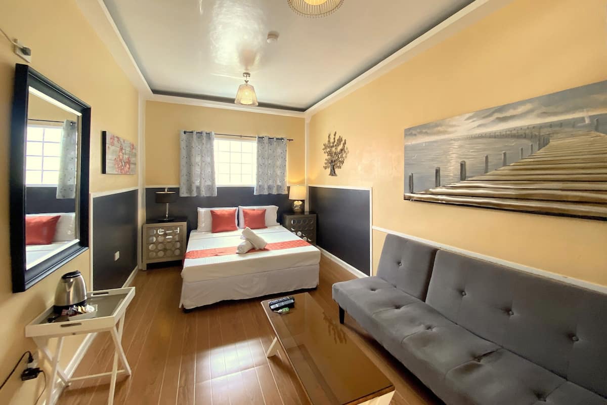 Une chambre à coucher avec un lit, un canapé, un bureau, une lampe, un tableau et un ventilateur de plafond.