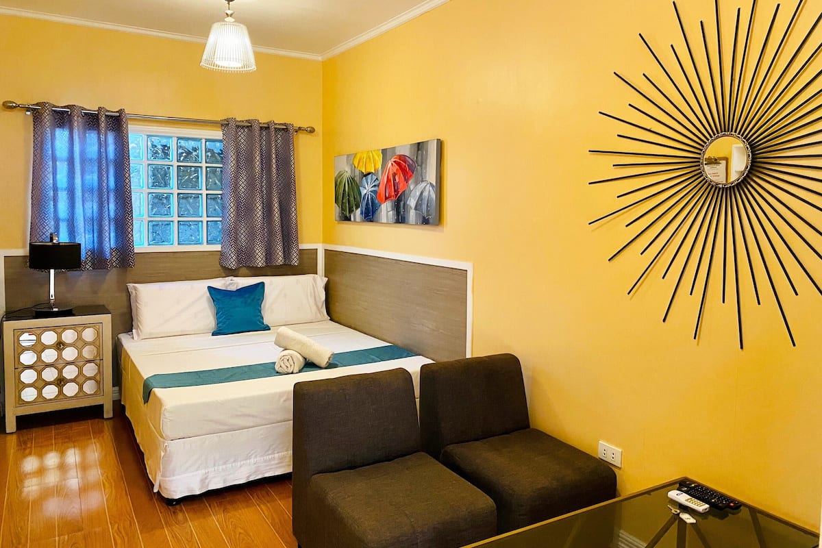 Une chambre à coucher comprenant un lit, une table de chevet, une lampe, un canapé, une table en verre et un miroir fixé au mur.