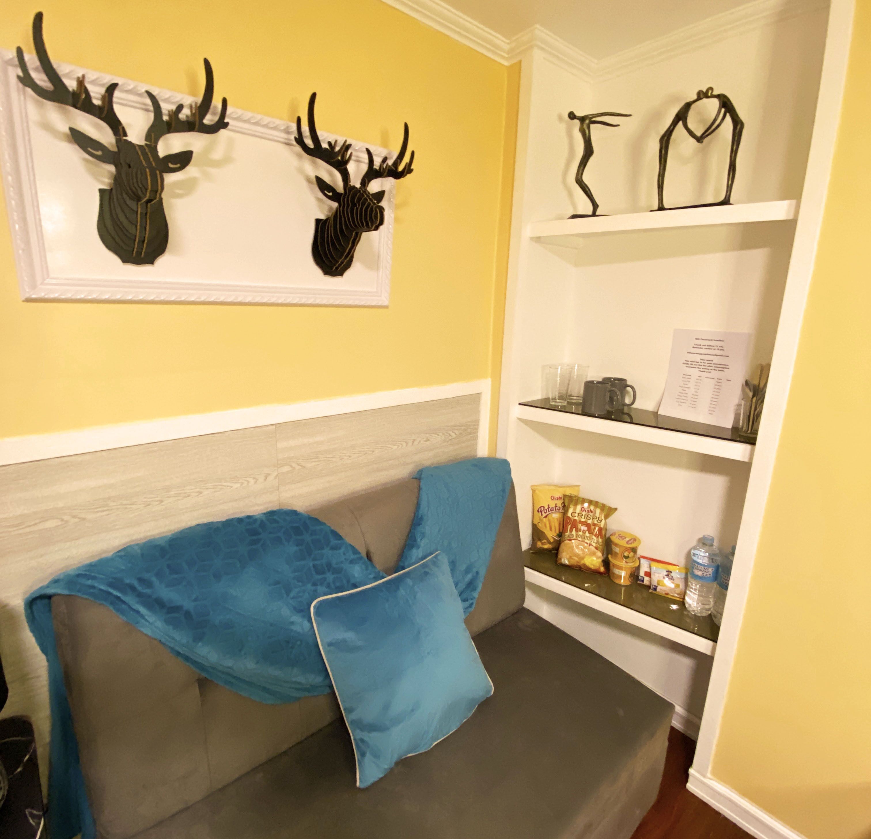 A room with a grey sofa, a blue throw blanket, and a shelf with snacks and a water bottle.