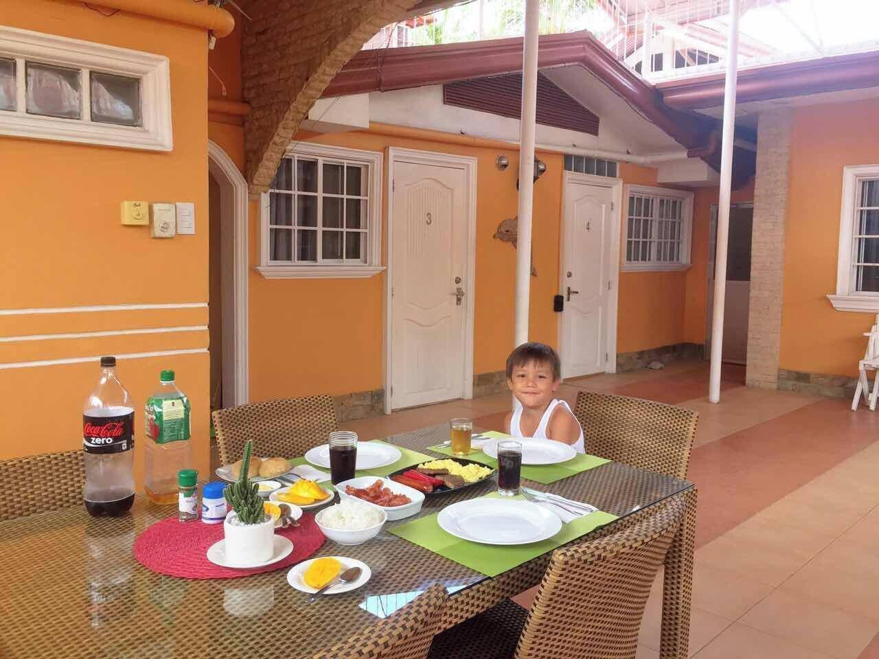 A dining table with breakfast items, a bottle of Coca-Cola Zero, and a child seated at the table.