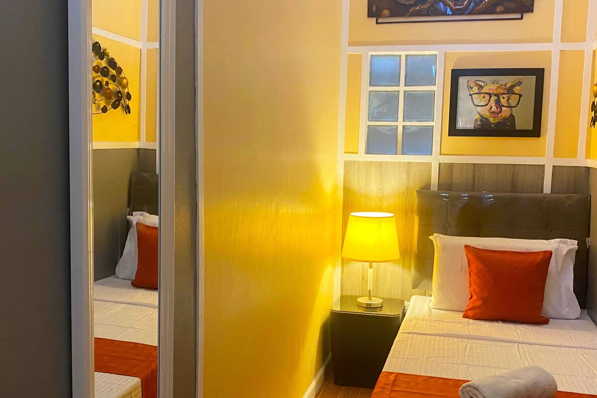 Une chambre d’hôtel avec un lit, une table de chevet, une lampe, un miroir et des œuvres d’art accrochées aux murs.
