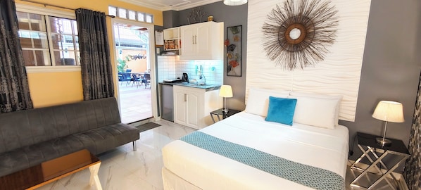 A hotel room with a bed, a sofa, a kitchenette, and a view of the outside. - Little Norway guest house - Close to airport (Lapu-Lapu)