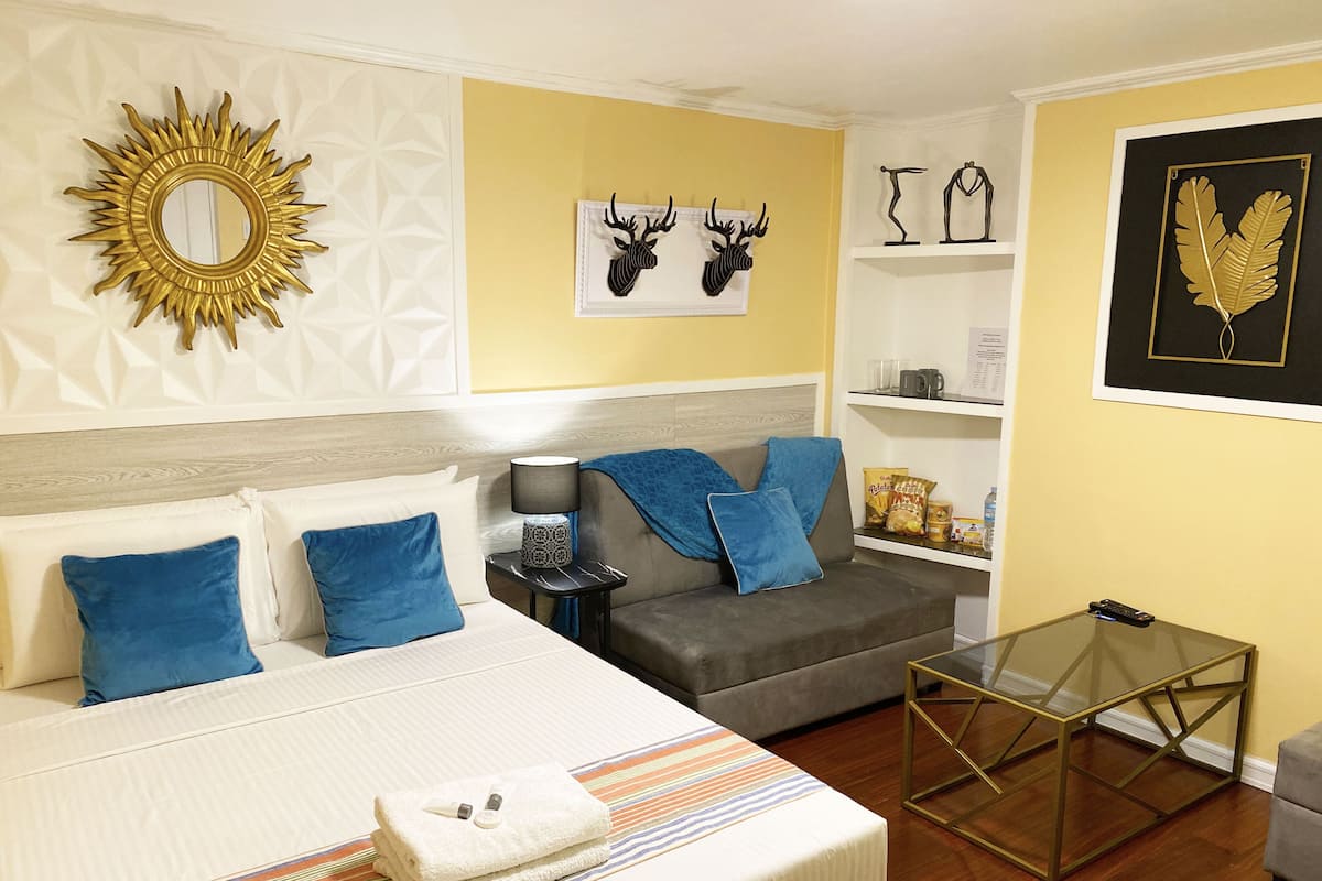 Une chambre d’hôtel comprenant un lit, un canapé, une table basse en verre et des œuvres d’art décoratives accrochées au mur.