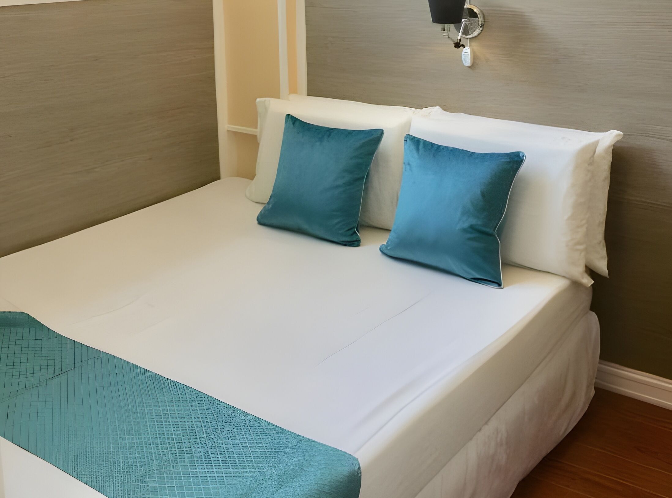 Una cama impecablemente arreglada con ropa de cama blanca y turquesa, un plaid turquesa y una lámpara de pared.