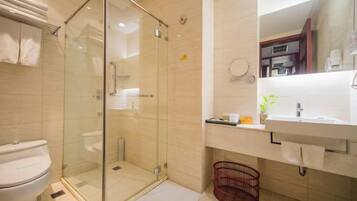 A modern bathroom with a glass-enclosed shower, a white toilet, a sink with a mirror, and a red basket.