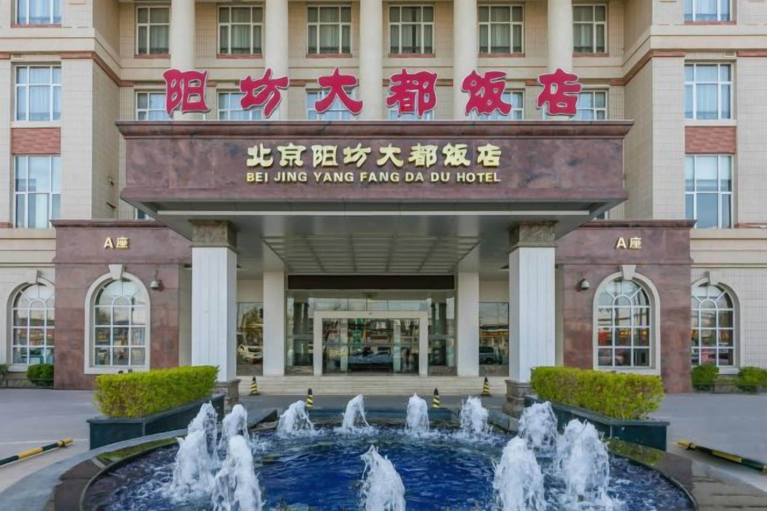 A hotel entrance with a fountain in front, large windows, and a sign in a foreign language.