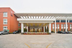 A hotel entrance with a covered walkway, a parking area, and a red building to the left. - Yangfang Dadu Hotel (Beijing)