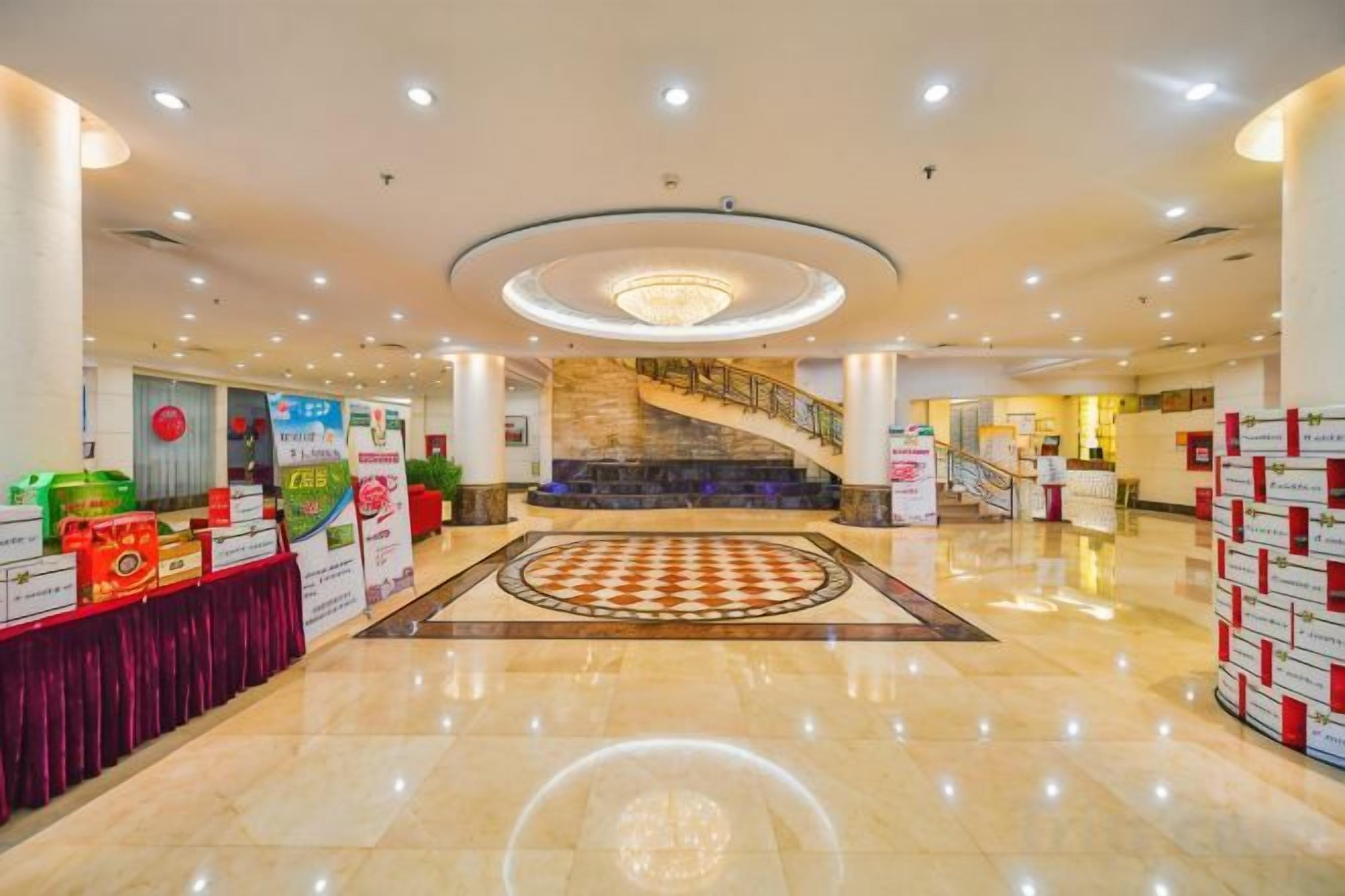 A spacious lobby with a central staircase, a chandelier, and a checkered floor pattern.