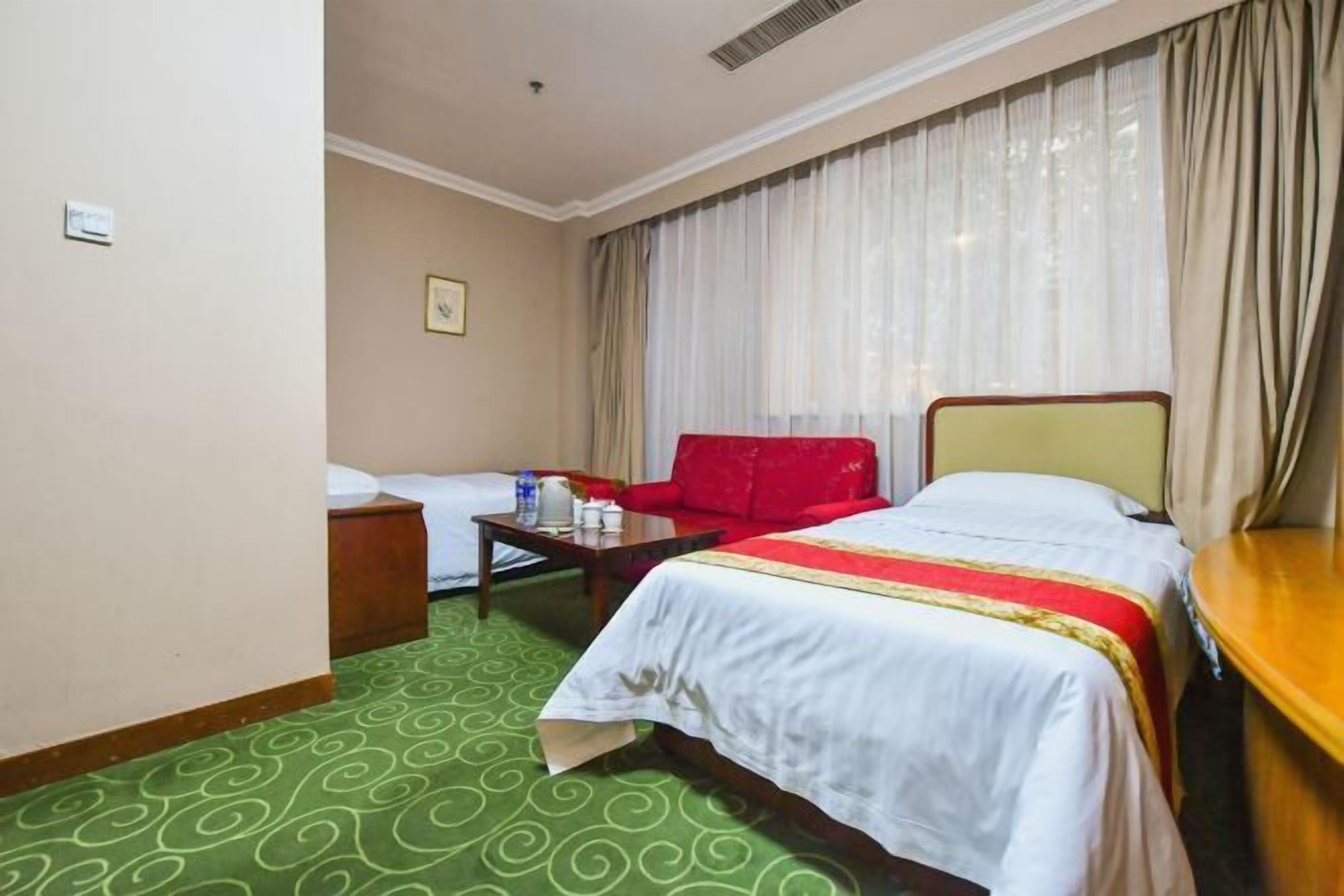 Una habitación de hotel con una cama, un sillón rojo, una mesita y una ventana con cortinas.