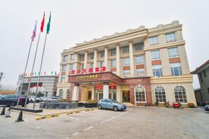 A hotel with a prominent entrance, multiple flags, and a parking lot. - Yangfang Dadu Hotel (Beijing)