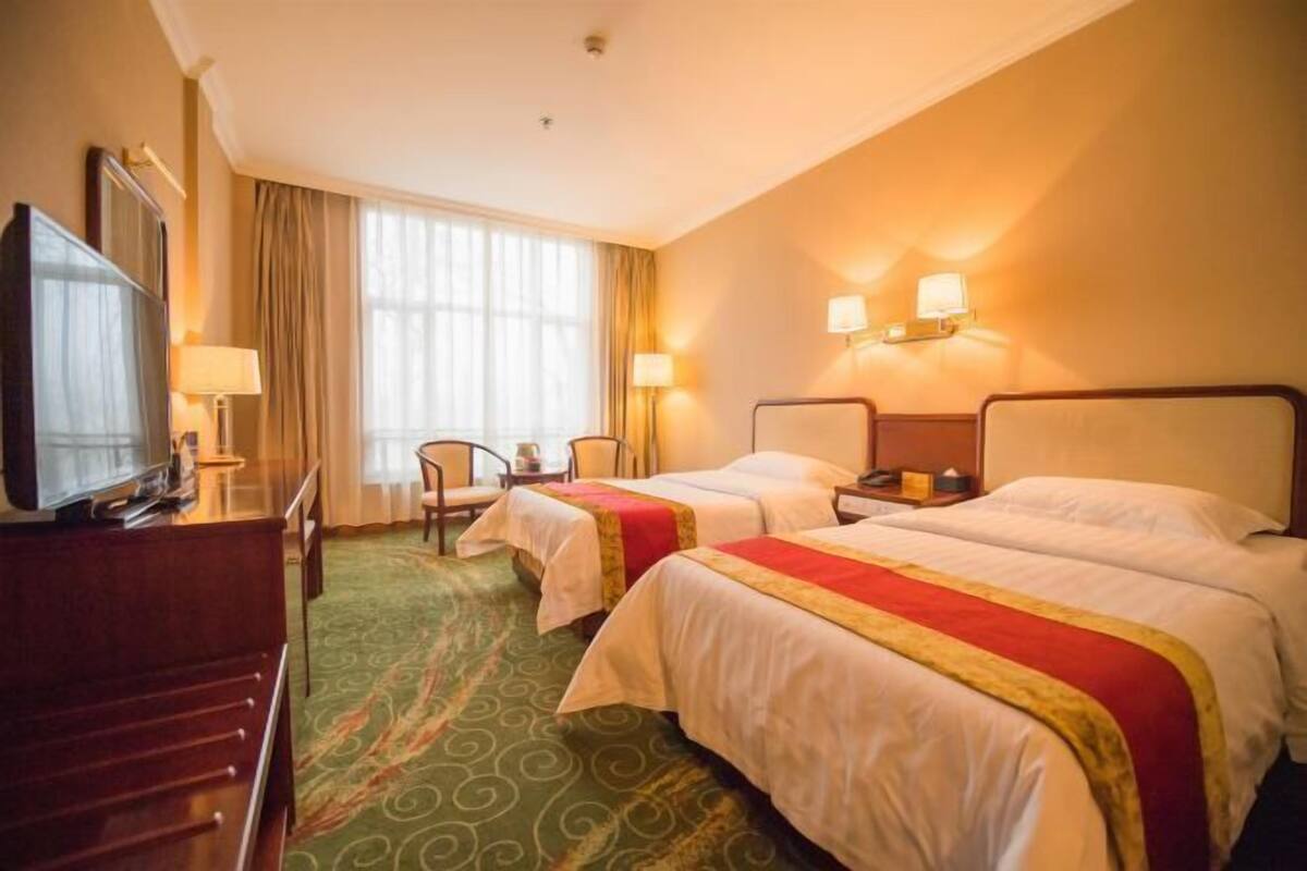 A hotel room with two beds, a TV, a desk, and a chair.