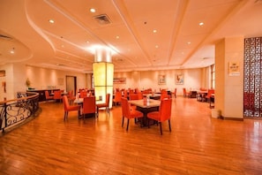A spacious dining area with multiple tables and chairs, a central pillar, and a decorative wall. - Yangfang Dadu Hotel (Beijing)