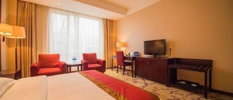 A hotel room with a large bed, two red chairs, a desk with a television, and a window with curtains.