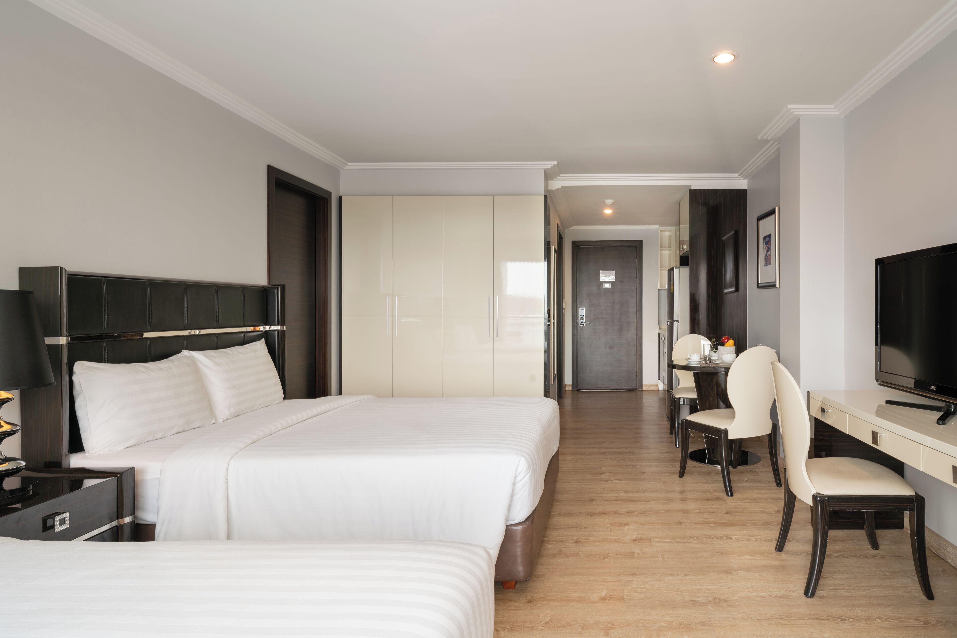 A hotel room with two beds, a desk, a chair, a television, and a wardrobe.