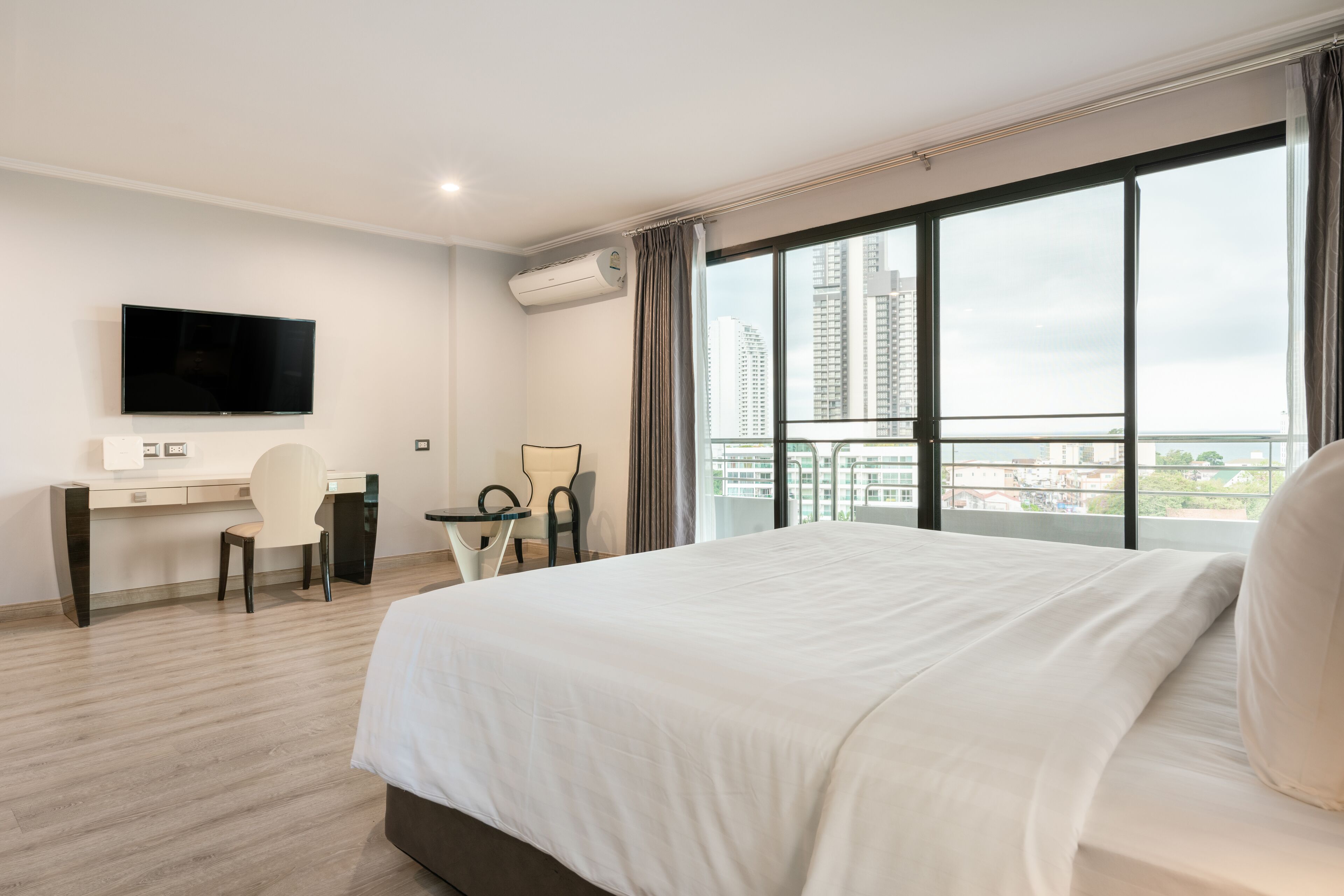 Een moderne hotelkamer met een groot bed, een bureau, een stoel, een flatscreen televisie en een balkon met uitzicht op de stad.