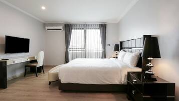 Hotellihuone, jossa on sänky, työpöytä tuolilla, televisio ja yöpöytä lampun kanssa.