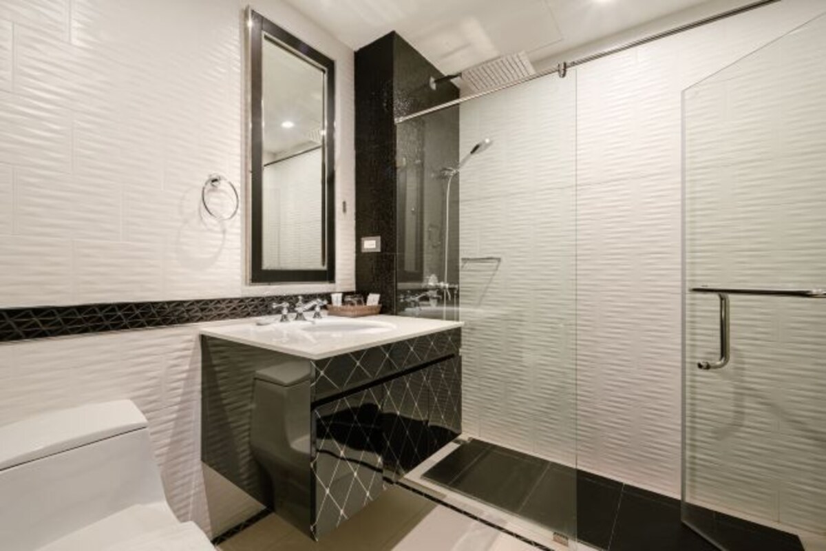 A modern bathroom with a glass-enclosed shower, a white sink with a black countertop, and a large mirror above the sink.