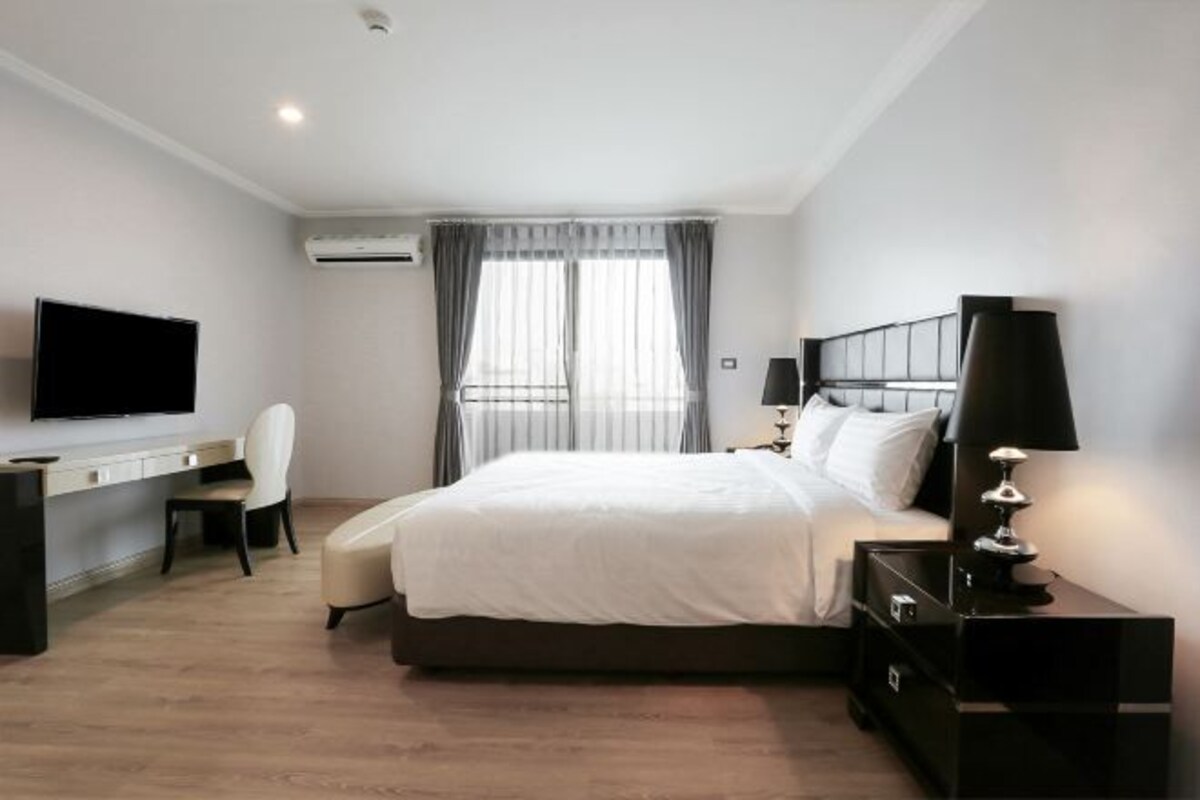A hotel room with a bed, a desk, a chair, a TV, and a lamp.