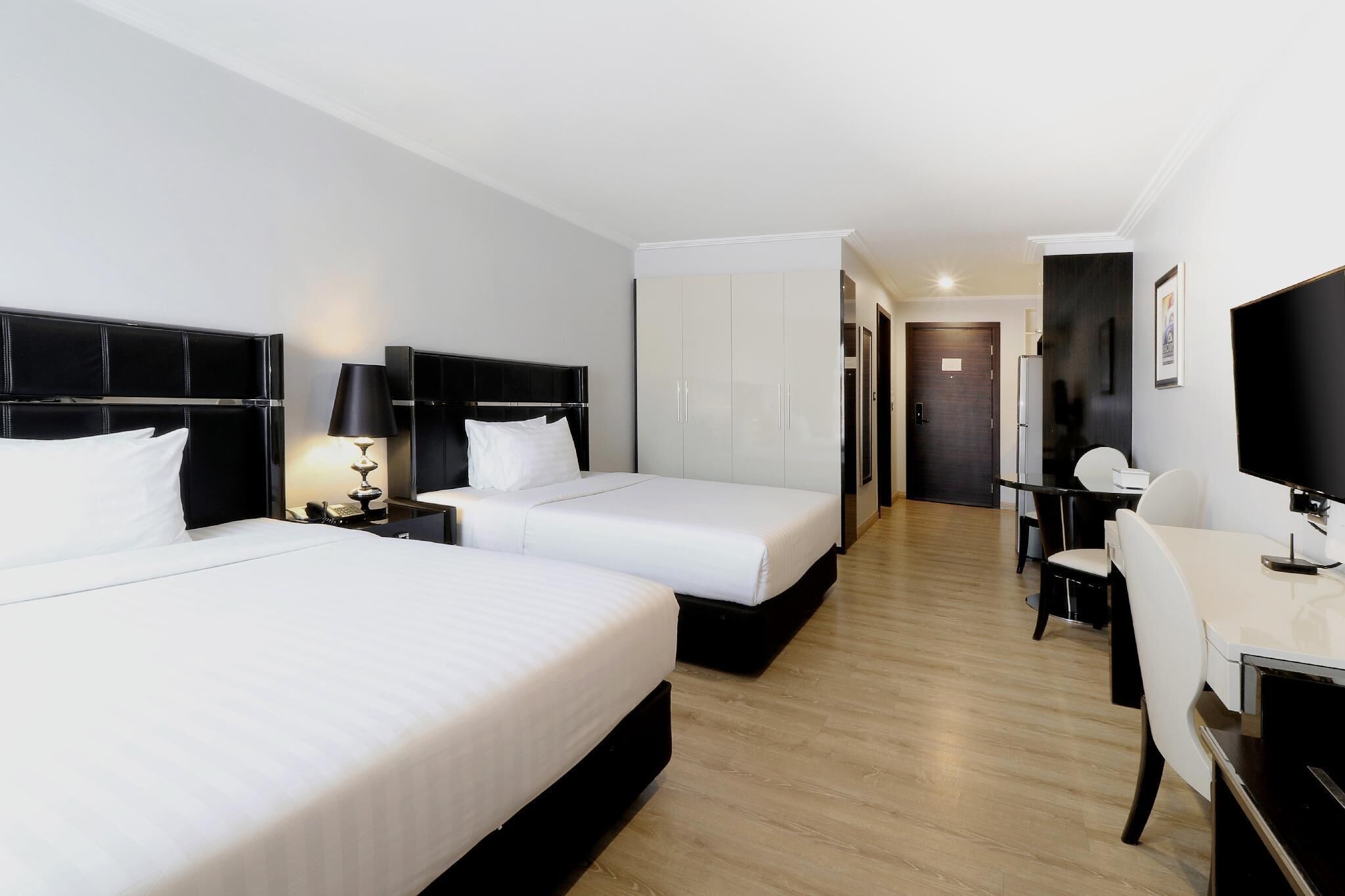 A hotel room with two beds, a desk, and a TV.
